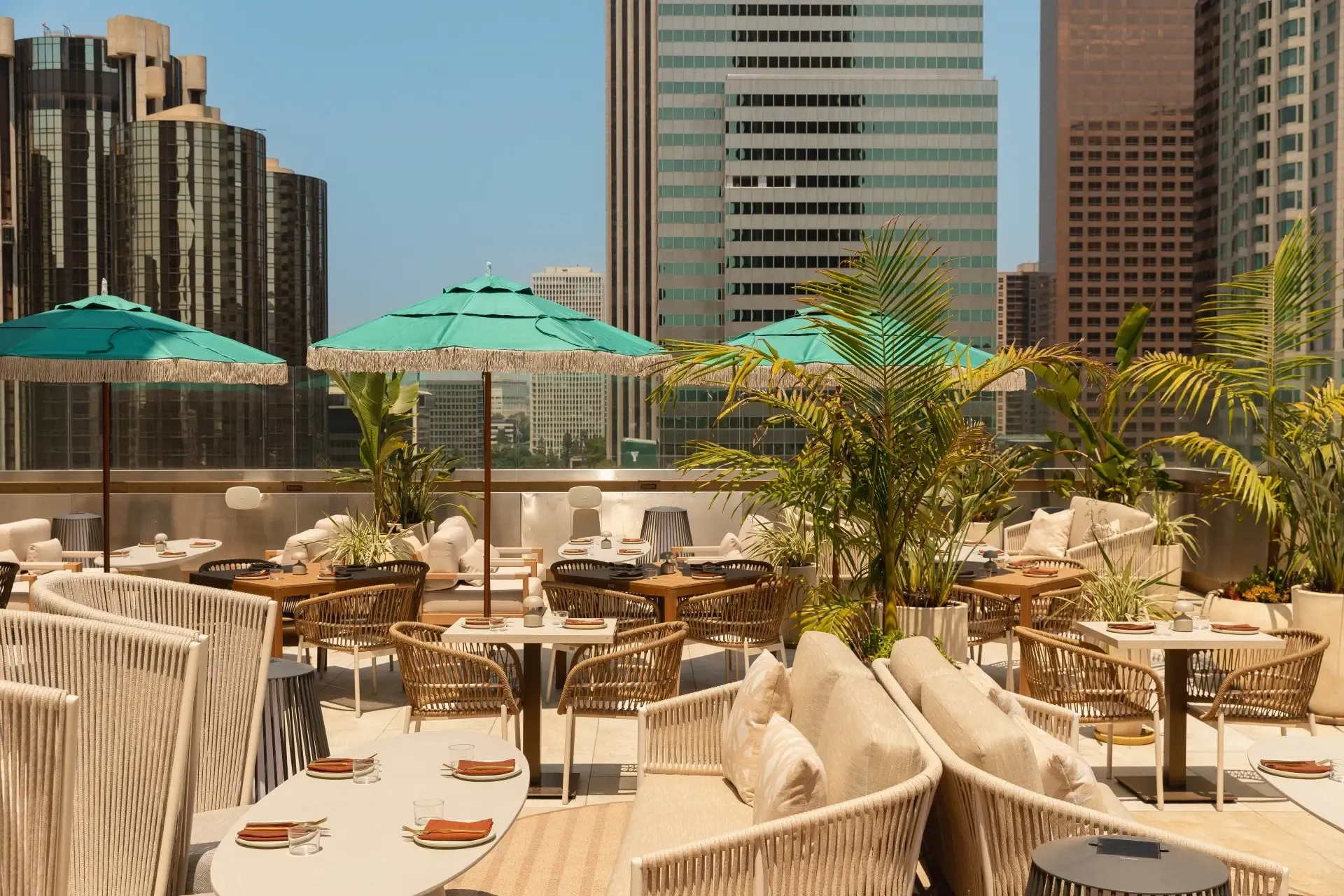 Rooftop terrace dining with rope lounge seating and teal fringed umbrellas above downtown Los Angeles